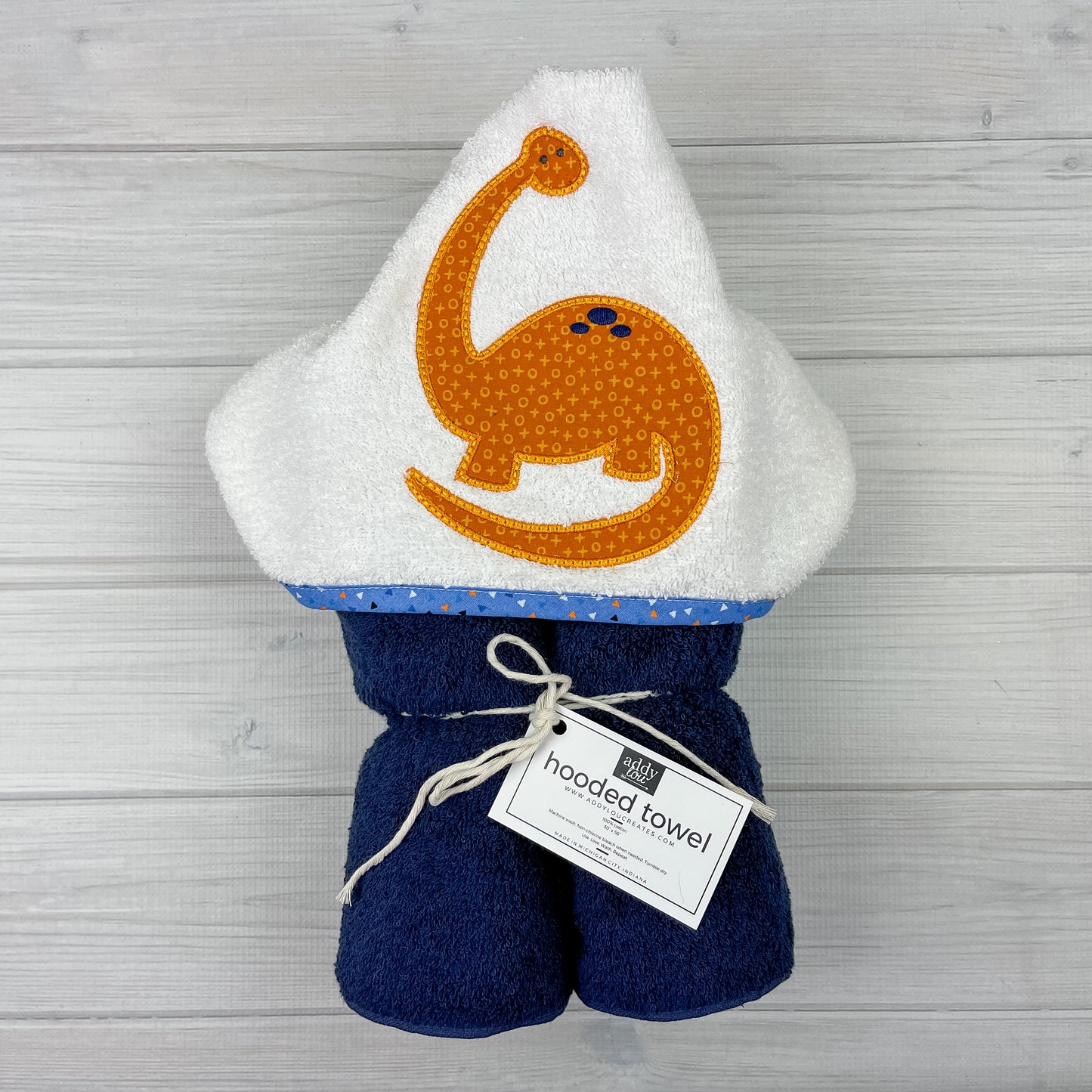 Navy blue hooded towel with orange brontosaurus embroidered on a white hood. Binding is medium blue with orange, white, and black triangles.