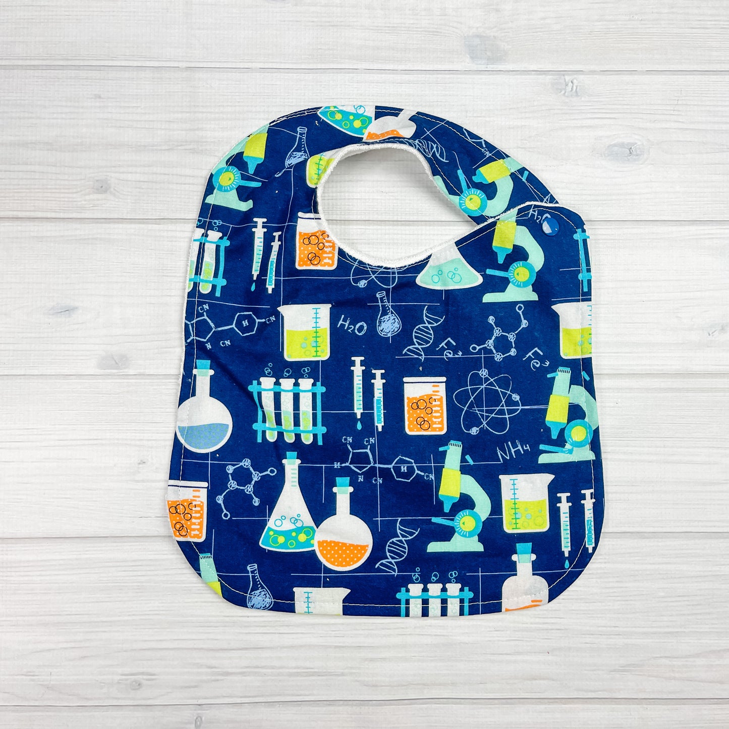 generously sized infant/toddler bib. Navy blue background with science symbols, microscopes and beakers in aqua blue and lime green.