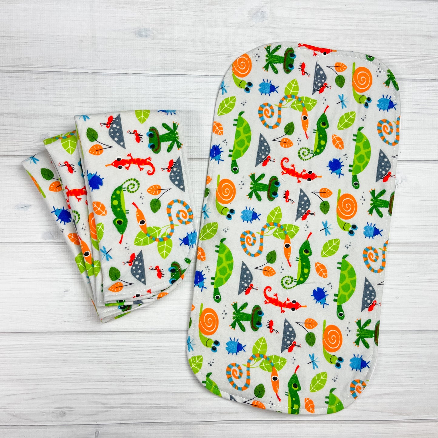 gray flannel burp cloths with various bugs, snakes, lizzards, snails, ans leaves in greens, blues, oragnges, dark gray and reds.