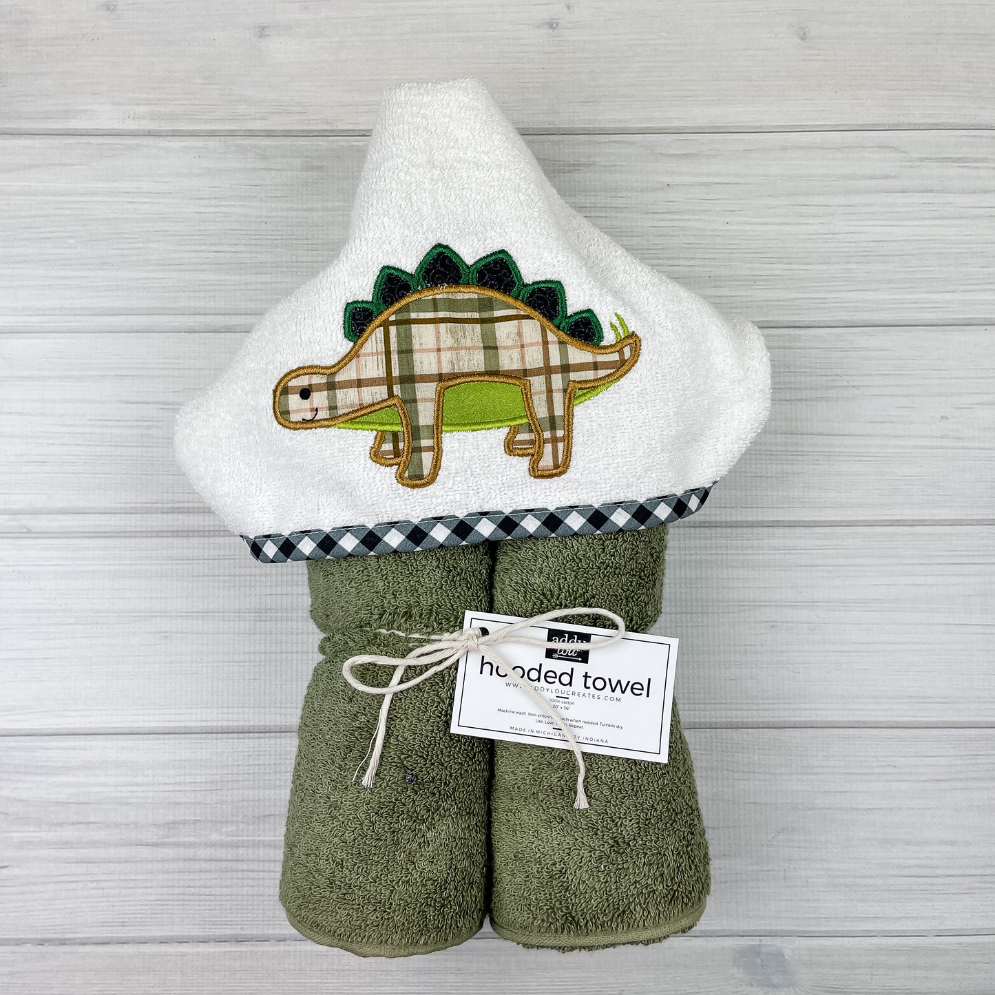 Sage green hooded towel with a brown & green plaid Stegosaurus embroidered.  Binding is black and white buffalo check.