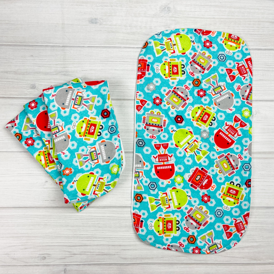 Flannel Burp cloths with robots in various sizes and shapes. Robots colors are in gray, lime green and red.  The aqua blue background has nut in shades of red, orange and white. 