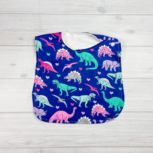 Generously sized infant/toddler bib. navy blue back ground with purple, teal pink and gray dinosaurs and hearts 