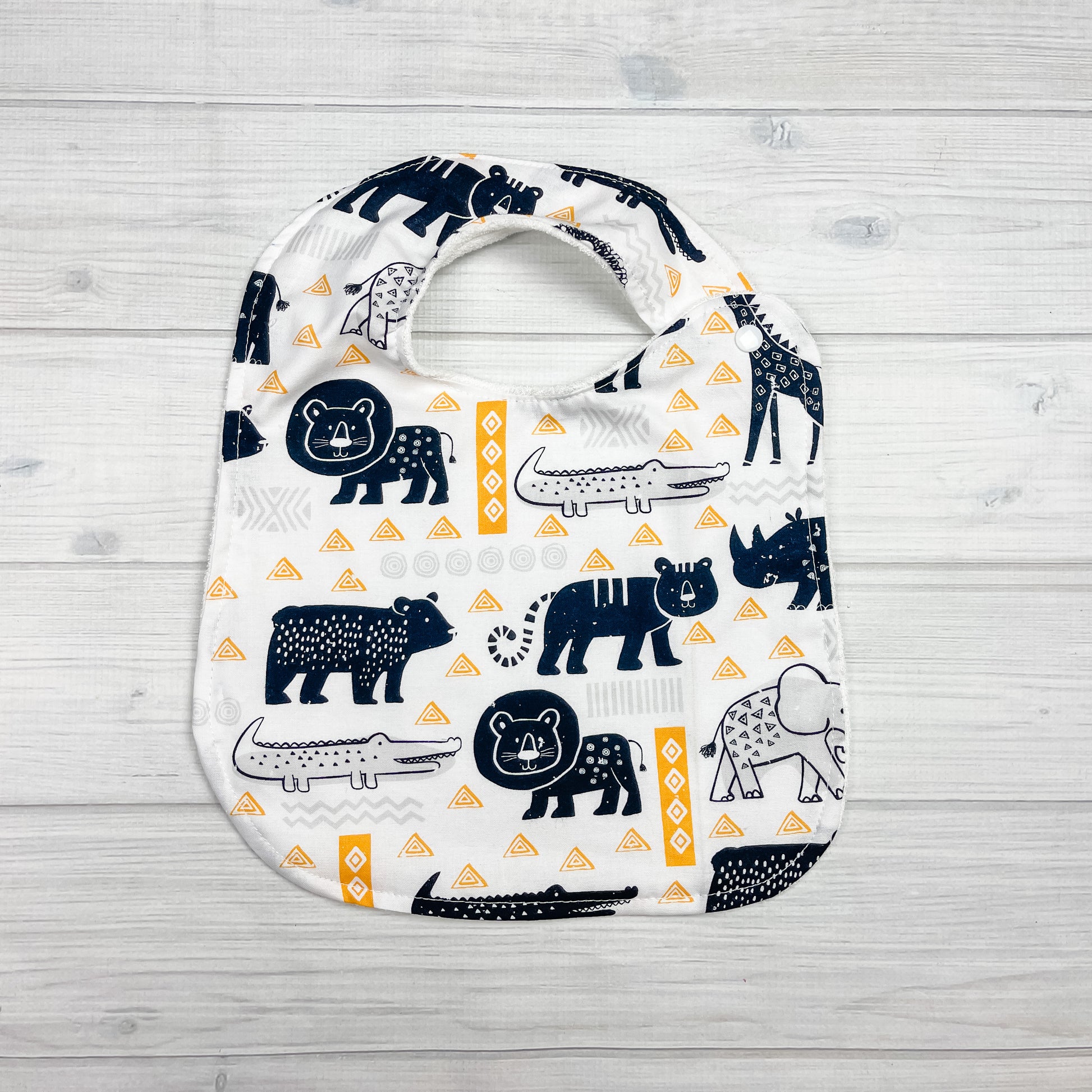 Generously sized infant/toddler bib. White background with black and white lions, giraffes, alligators, elephants and bears. accented with yellow and light gray geometric shapes. 