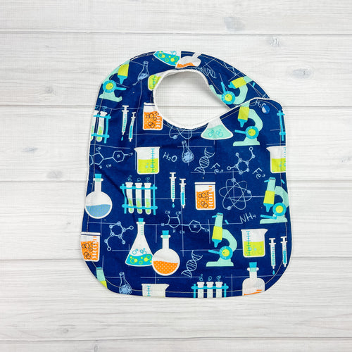 generously sized infant/toddler bib. Navy blue background with science symbols, microscopes and beakers in aqua blue and lime green. 