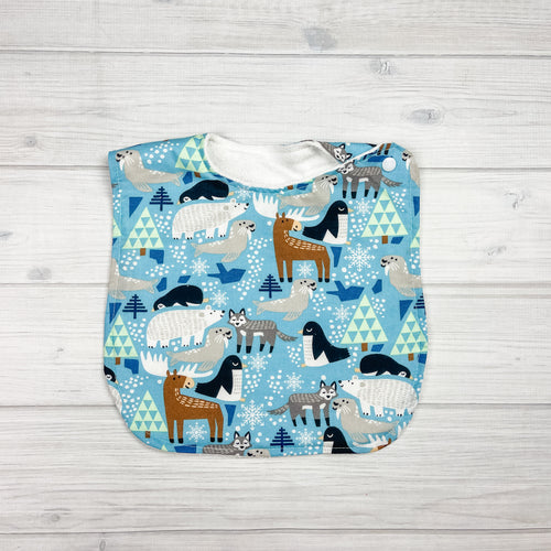 Generously sized infant/toddler bib. Light blue background with snowflakes & trees. Animals include seals, moose, pengiuns, polar bears, and wolves